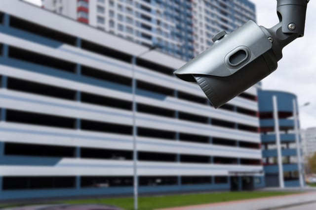 Dark grey bullet CCTV camera on a bracket overlooking a residential parking building