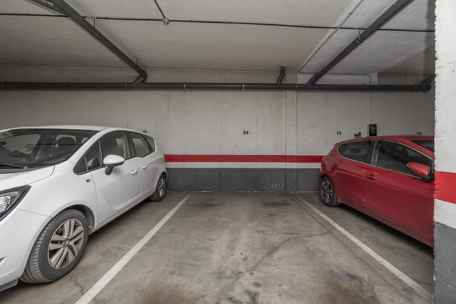 Empty numbered parking bay between a white car and a red car in a residents' undercroft car park