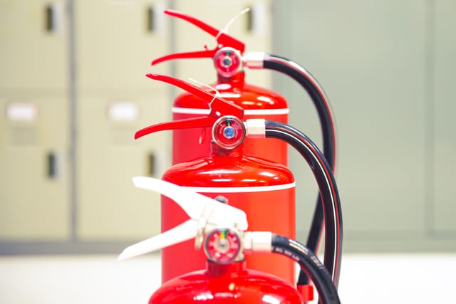 Row of red fire extinguishers with pressure gauges and black hoses