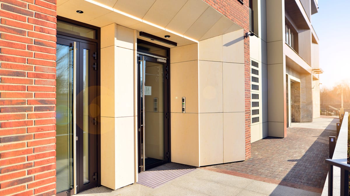 Glazed communal entrance of a red brick apartment building with a paved approach.