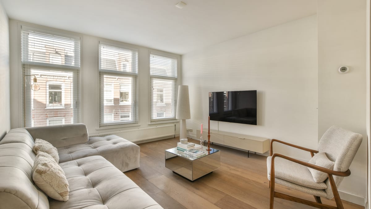 Apartment living room with a greige sofa, warm oak floor and three tall windows.