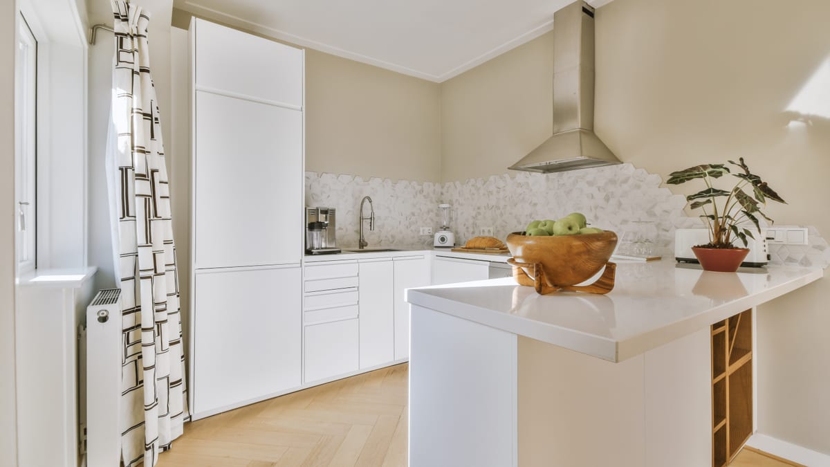 Fitted apartment kitchen with white units, a peninsula and a light oak herringbone floor.