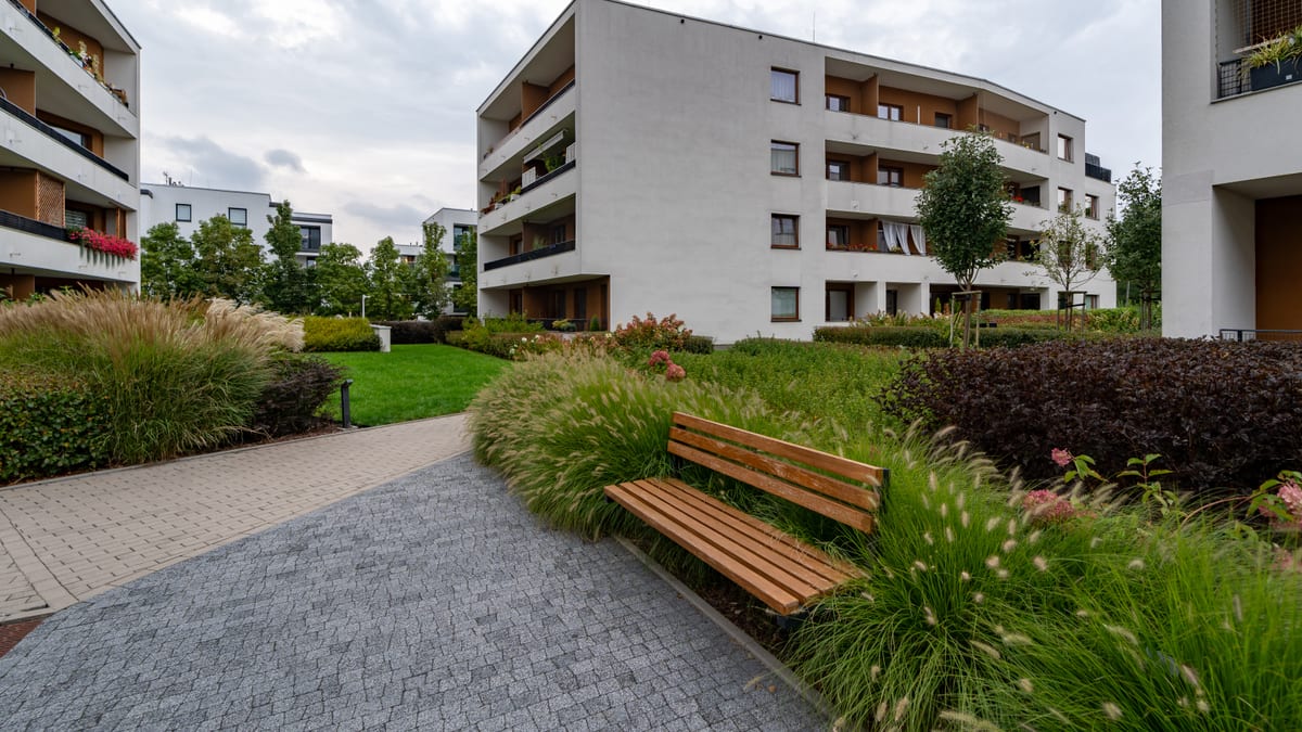 Landscaped courtyard between apartment blocks with a timber bench and clipped planting.