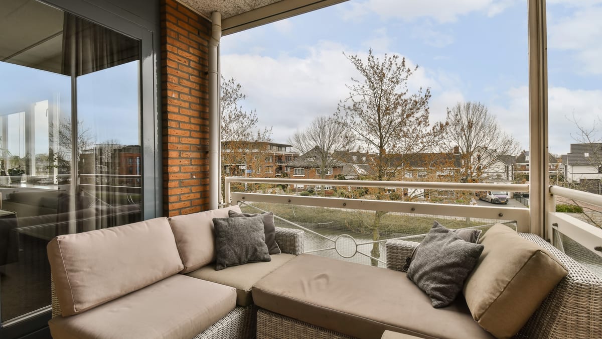 Apartment balcony with wicker seating, cushions and a low table.